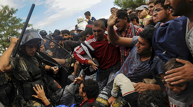 Un policía amenaza a los refugiados para impedirles la entrada Macedonia en la frontera con Grecia.