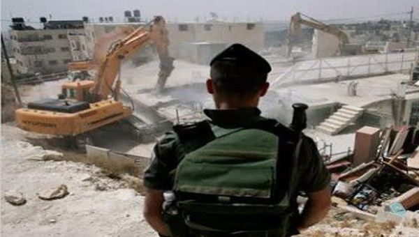 Soldado israelí viendo una excavadora destruye una  casa palestina. (Foto: Maan)