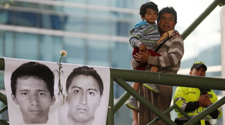 Un padre carga a su pequeño hijo al lado de una foto de los estudiantes desaparecidos durante las protestas.