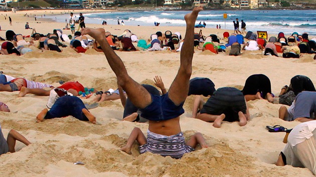 Entierran sus cabezas en una playa australiana contra el cambio climático. (Reuters)