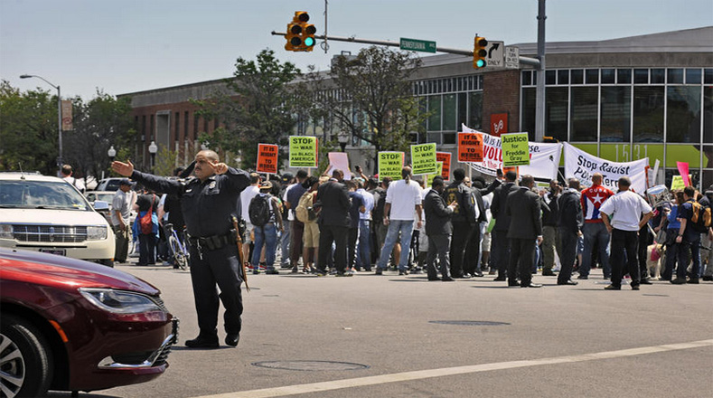 Un policía de Baltimore dirige el tráfico alrededor de los manifestantes, quienes van camino a un mitin frente a la alcaldía.